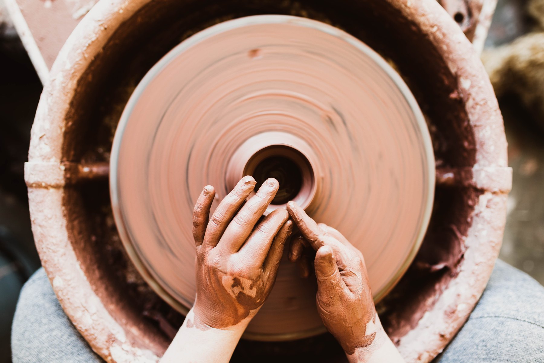 Clay-covered hands centering a pot on a spinning wheel. Photograph by Jared Sluyter, public domain.